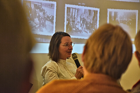 Kristina Vagt erläutert die Deportationsfotos, hinter ihr drei schwarzweiß Fotografien auf einer Leinwand