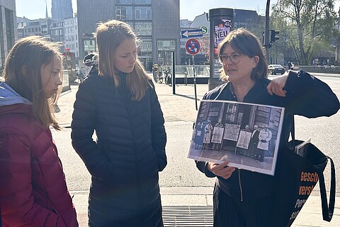 Eine Mitarbeiterin des Geschichtsort Stadthaus zeigt Teilnehmenden ein historisches Foto beim Rundgang.